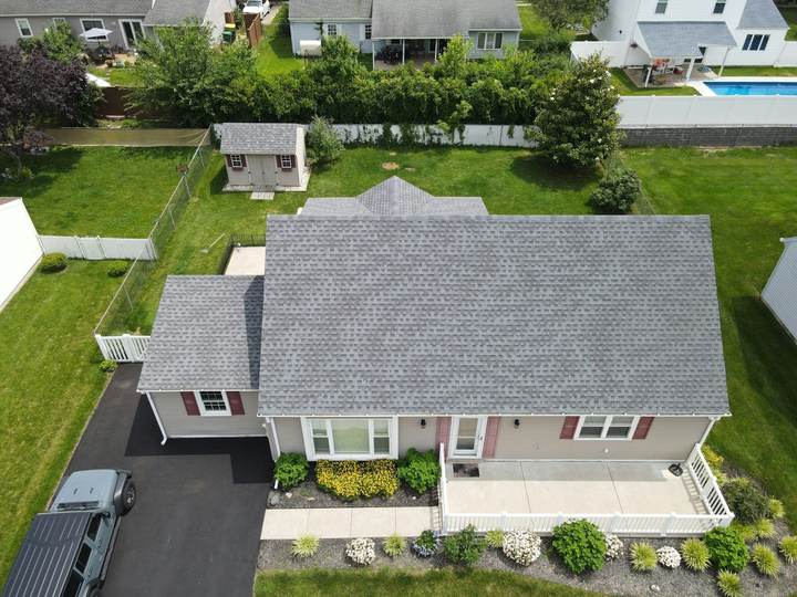Aerial drone view of a single-storey house with a grey asphalt shingle roof and its surrounding yard.